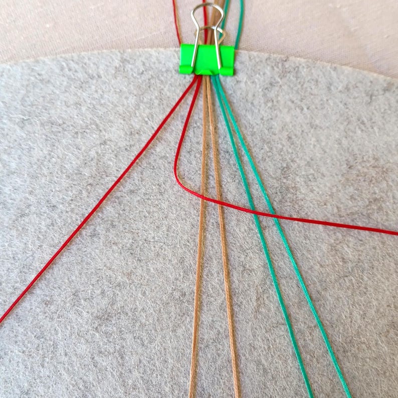 K&ouml;nnte beinhalten: Nahaufnahme eines roten, braunen und t&uuml;rkisfarbenen Armbands aus Schnur, das mit einer gr&uuml;nen B&uuml;roklammer hergestellt wird, die die Schn&uuml;re an Ort und Stelle h&auml;lt.