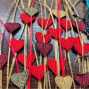 Pode incluir: Uma cole&ccedil;&atilde;o de pingentes feitos &agrave; m&atilde;o em forma de cora&ccedil;&atilde;o com fio vermelho e dourado. Os pingentes s&atilde;o enfiados em cord&otilde;es dourados e s&atilde;o perfeitos para adicionar um toque de charme artesanal a qualquer projeto.