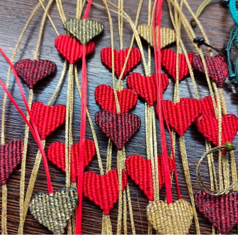 Pode incluir: Uma cole&ccedil;&atilde;o de pingentes feitos &agrave; m&atilde;o em forma de cora&ccedil;&atilde;o com fio vermelho e dourado. Os pingentes s&atilde;o enfiados em cord&otilde;es dourados e s&atilde;o perfeitos para adicionar um toque de charme artesanal a qualquer projeto.