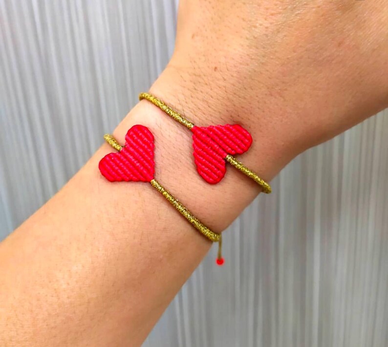 Pode incluir: Um bracelete dourado com dois pingentes de cora&ccedil;&atilde;o vermelho. O bracelete &eacute; feito de um cord&atilde;o fino e tran&ccedil;ado.