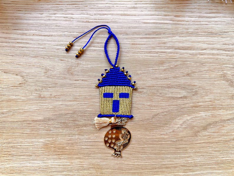 Pu&ograve; includere: Un ornamento in macram&egrave; blu e oro con un design a croce e un ciondolo a forma di melograno dorato. L'ornamento &egrave; appeso a un cordoncino blu.