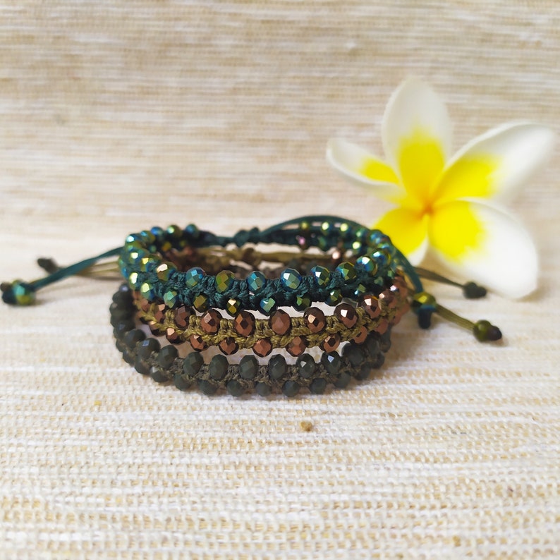 May include: A set of three beaded bracelets in shades of green and brown. The bracelets are made with small, iridescent beads and are tied together with a cord.