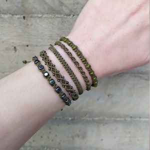 Puede incluir: Cinco pulseras apiladas en una muñeca. Las pulseras están hechas de cordón verde y tienen pequeñas cuentas verdes y gris oscuro.