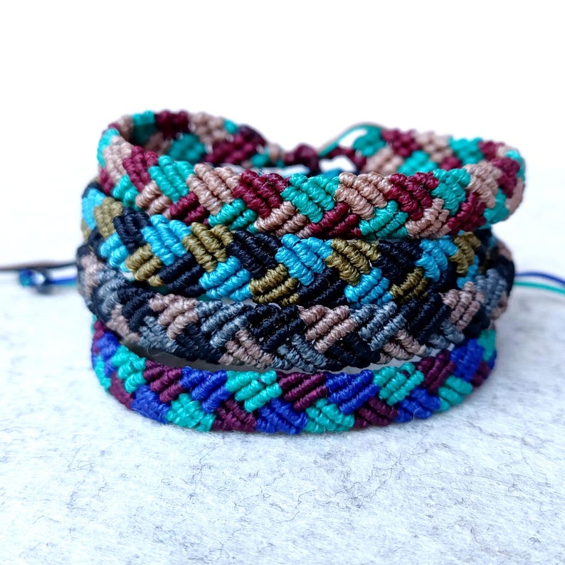 K&ouml;nnte beinhalten: Vier bunte Freundschaftsarmb&auml;nder mit einem Chevron-Muster. Die Armb&auml;nder sind aus gewebtem Garn in den Farben Blau, Gr&uuml;n, Braun, Schwarz und Rot.