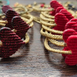 Pode incluir: Dois conjuntos de pulseiras em forma de cora&ccedil;&atilde;o, um conjunto em vermelho e outro em bord&ocirc;. As pulseiras s&atilde;o feitas de fio tecido e s&atilde;o enfiadas em um cord&atilde;o dourado.