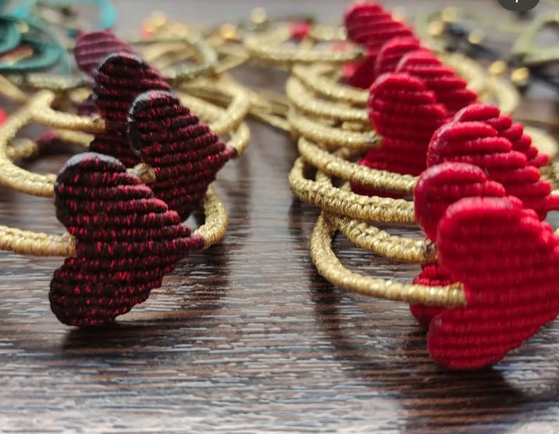 Pode incluir: Dois conjuntos de pulseiras em forma de cora&ccedil;&atilde;o, um conjunto em vermelho e outro em bord&ocirc;. As pulseiras s&atilde;o feitas de fio tecido e s&atilde;o enfiadas em um cord&atilde;o dourado.