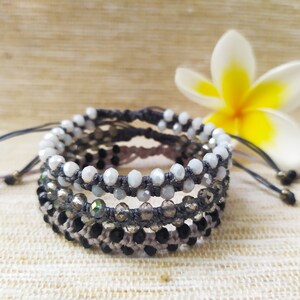 May include: A set of four bracelets with gray cord and various colored beads. The bracelets are layered on top of each other and feature white, black, and iridescent beads.