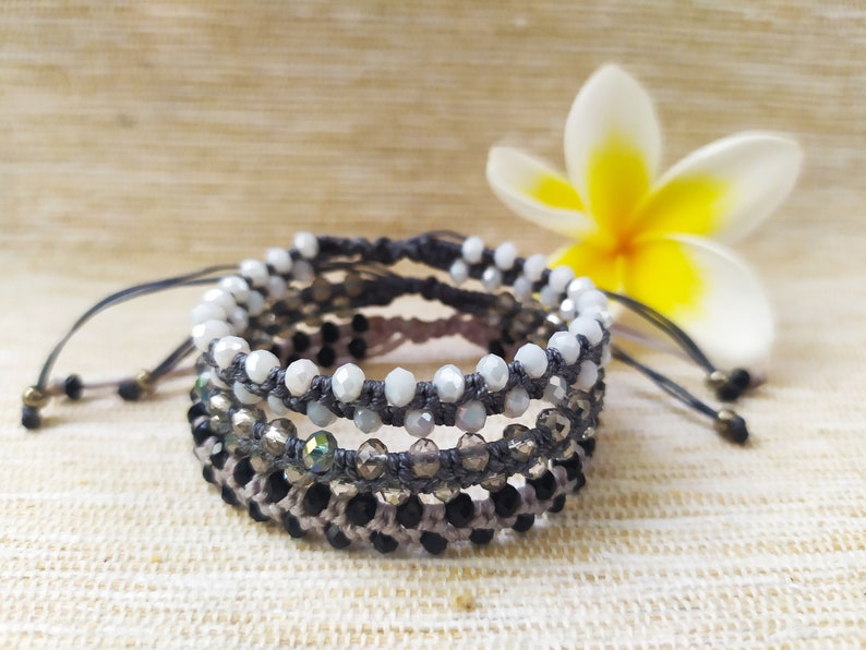 May include: A set of four bracelets with gray cord and various colored beads. The bracelets are layered on top of each other and feature white, black, and iridescent beads.
