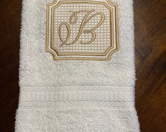 May include: White hand towel with a gold embroidered monogram of the letter "B" in a square frame.