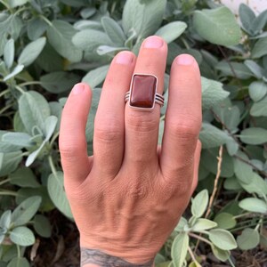 May include: A silver ring with a rectangular brown gemstone. The ring has three bands.