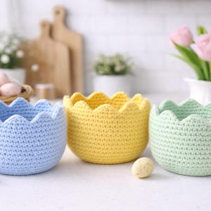 Pode incluir: Três tigelas de crochê feitas à mão em cores pastel: azul claro, amarelo e verde menta. Cada tigela tem uma borda ondulada. As tigelas são provavelmente para decoração de Páscoa ou primavera. As tigelas têm cerca de 10 cm de diâmetro.