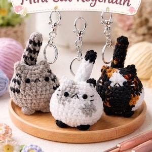 May include: Crochet mini cat keychains in gray, white, and calico patterns. Each keychain features a silver ring and a small, round cat design with a tail. The text "Crochet Mini Cat Keychain" is displayed above the keychains.