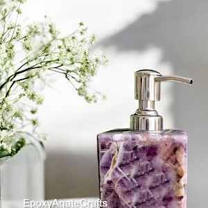 May include: Purple amethyst soap dispenser with a silver pump. The dispenser is made of natural stone and has a unique, organic look.