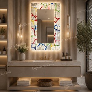 May include: A modern bathroom vanity with a rectangular mirror. The mirror frame features a colorful, mosaic-like design with red, blue, yellow, and green accents. The vanity has a neutral color scheme with a floating design and a lower shelf.
