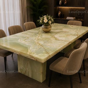 May include: A rectangular dining table featuring a polished light green onyx stone top with natural veining and a matching solid stone pedestal base, surrounded by eight upholstered beige chairs with vertical channel tufting and black legs.
