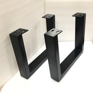 May include: Two black metal table legs with a U-shaped design. The legs are made of sturdy metal and have a black powder coat finish.