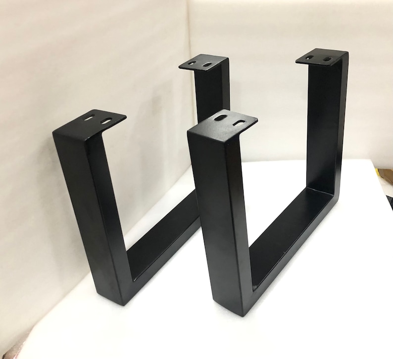 May include: Two black metal table legs with a U-shaped design. The legs are made of sturdy metal and have a black powder coat finish.