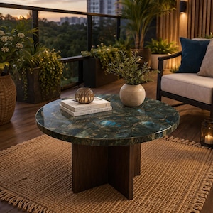 May include: A circular coffee table with a dark green and gold patterned surface and a dark brown wooden base. The table is on a woven rug, with a vase of greenery and books on top. The text "LIVE BEAUTIFULLY" is visible on the books.