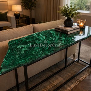 Puede incluir: Una consola moderna con una llamativa tapa verde malaquita y un marco de metal negro. La mesa presenta un patrón único y orgánico en su superficie, agregando un toque de lujo a cualquier espacio habitable. La mesa mide aproximadamente 122 cm de largo.