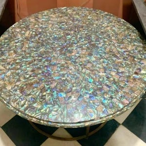 Könnte beinhalten: Ein runder Tisch mit einer Tischplatte aus schillernden Perlmutt-Fliesen. Der Tisch hat ein goldenes Metallgestell.