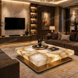 Puede incluir: Un lujoso salón con una gran mesa de centro cuadrada iluminada con una superficie similar al mármol y una base dorada. La habitación incluye un sofá seccional marrón, un televisor de pantalla plana grande y estanterías empotradas con objetos decorativos.