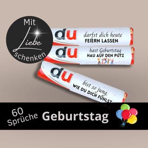 Puede incluir: Tres barras de caramelo envueltas en rojo y blanco con la palabra "du" impresa en ellas. Cada barra tiene un mensaje de cumpleaños diferente impreso en el envoltorio. Los mensajes son "darfst dich heute FEIERN LASSEN", "hast Geburtstag HAU AUF DEN PUTZ" y "bist so jung, WIE DU DICH FÜHLST". El texto "60 Sprüche Geburtstag" está impreso en una pancarta negra debajo de las barras de caramelo.