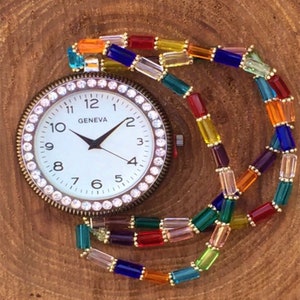 May include: A vintage-style pocket watch with a white face and a crystal-encrusted bezel. The watch is attached to a colorful beaded chain with rainbow-colored glass beads.