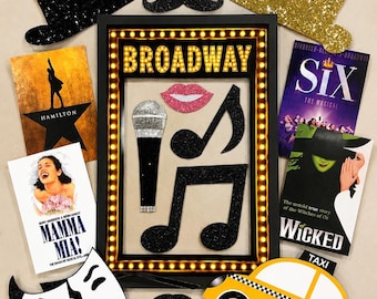 Puede incluir: Una colección de decoraciones para fiestas con temática de Broadway que incluye un letrero luminoso, sombreros de copa brillantes, recortes de notas musicales, un micrófono, un taxi amarillo, máscaras de teatro y carteles de musicales.