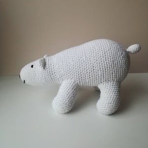 Può includere: Orso polare di peluche bianco lavorato a uncinetto. L'orso è in piedi su tutte e quattro le zampe con la testa girata di lato.