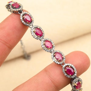 Puede incluir: Una pulsera de plata con un diseño de cadena y piedras preciosas rojas ovaladas engastadas en un halo de piedras preciosas blancas más pequeñas.