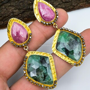 Peut inclure: Une paire de boucles d'oreilles pendantes avec une pierre précieuse rose et une pierre précieuse verte. Les boucles d'oreilles sont serties d'or et ont un halo de diamants autour de chaque pierre précieuse.