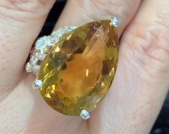 May include: A pear-shaped yellow gemstone ring set in silver with smaller gemstones around the band.
