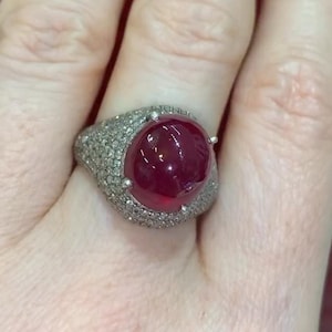 Può includere: Un anello d'argento con un grande rubino a cabochon circondato da diamanti più piccoli.