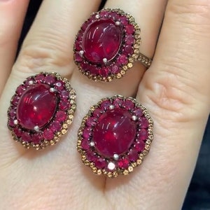 May include: A set of three rings featuring large oval cabochon ruby gemstones surrounded by a halo of smaller rubies and diamonds.
