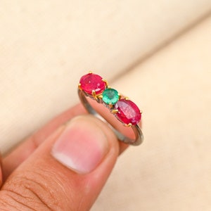 May include: A silver ring with three gemstones. The ring has two red oval-shaped gemstones and one green oval-shaped gemstone in the center.