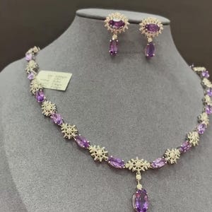 May include: A silver necklace and earrings set with a delicate floral design and oval-shaped amethyst gemstones. The necklace features a pendant with a larger amethyst gemstone.
