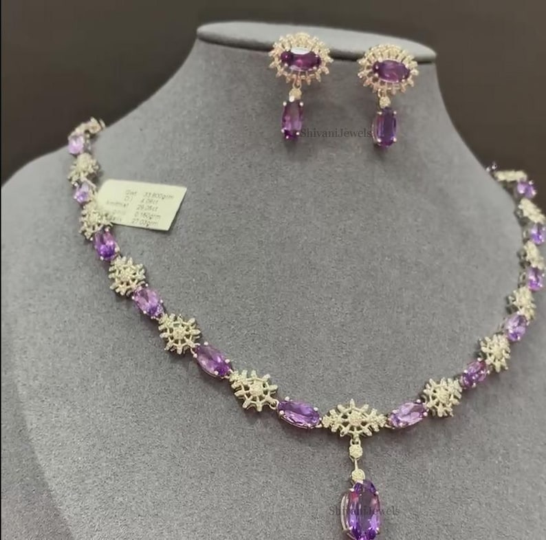 May include: A silver necklace and earrings set with a delicate floral design and oval-shaped amethyst gemstones. The necklace features a pendant with a larger amethyst gemstone.