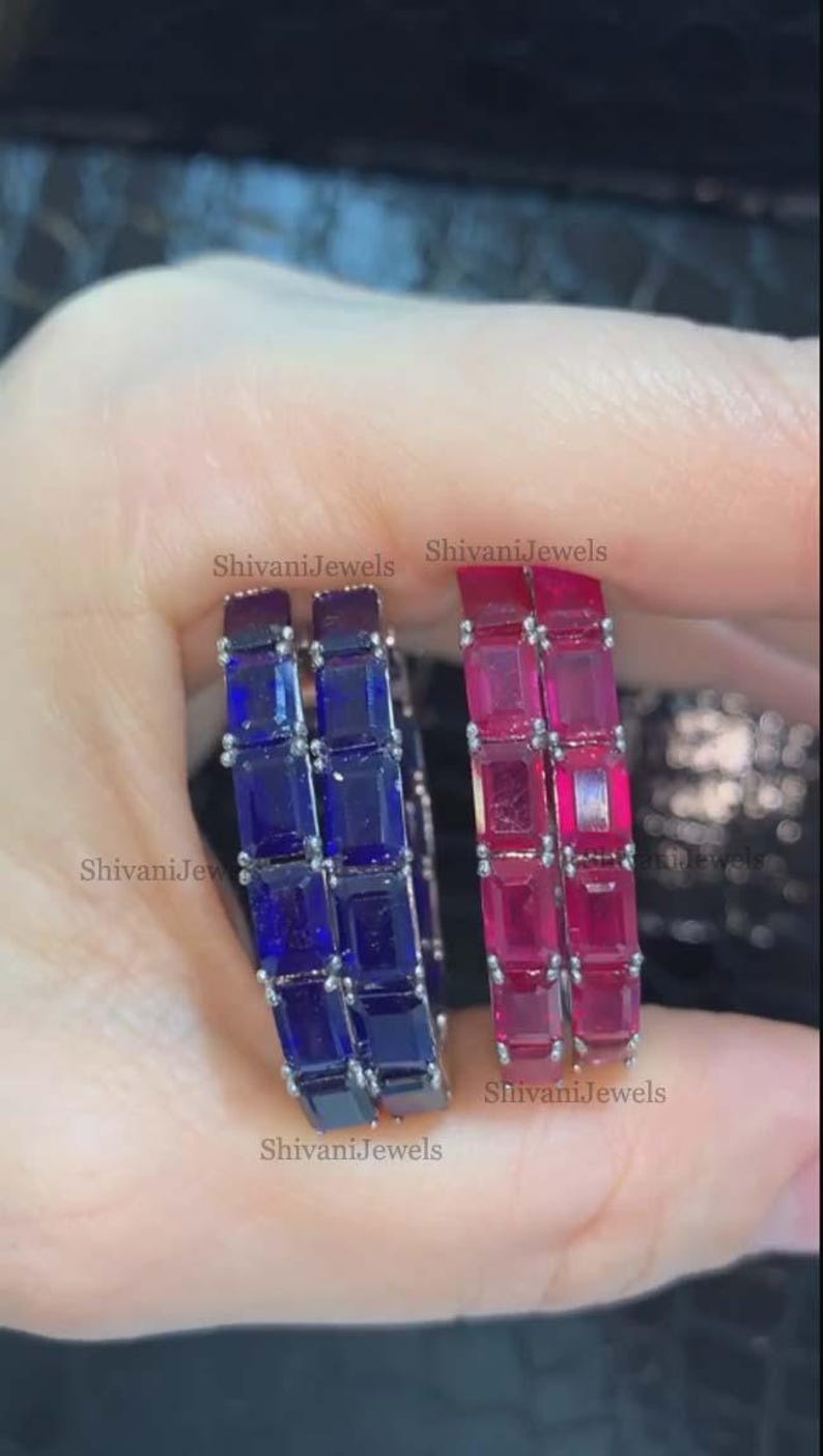 May include: Two pairs of gemstone hoop earrings. One pair features blue rectangular stones, the other features pink rectangular stones. The earrings are held in a hand. The text "ShivaniJewels" is visible on the image.