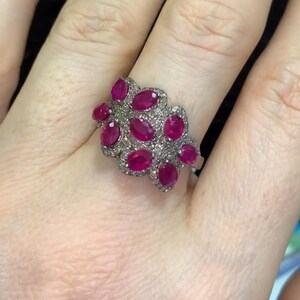 Peut inclure: Une bague en argent avec un groupe de pierres précieuses rubis de forme ovale et de petits diamants sertis dans un motif floral.