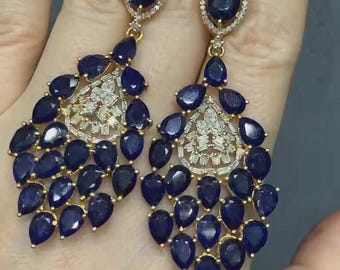 May include: A pair of dangle earrings with a teardrop design. The earrings are made of gold and feature a cluster of blue sapphire stones and clear diamonds.
