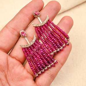 Op de afbeelding: Een paar oorhangers met een roze edelsteen aan de bovenkant en een franje van roze kralen en kleine diamanten.