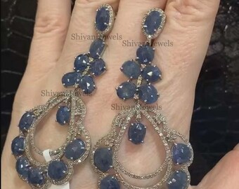 May include: A pair of dangle earrings with a silver setting and blue sapphire stones. The earrings feature a teardrop design with a cluster of smaller stones at the top.