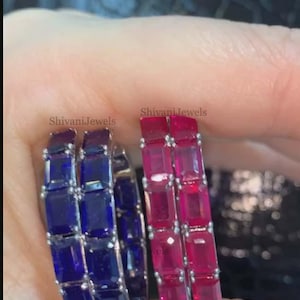 May include: Two pairs of hoop earrings, one with deep blue rectangular stones and the other with bright red rectangular stones. The earrings are set in a silver metal. The brand name "Shivani Jewels" is printed on the image.