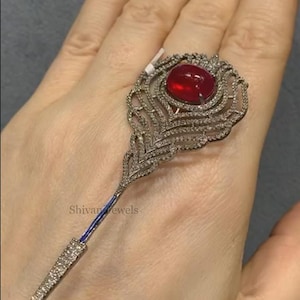 May include: A silver ring with a red gemstone and a peacock feather design. The ring is set with small diamonds.