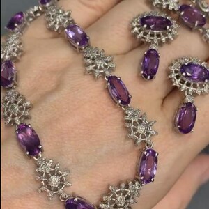 May include: A silver necklace and earrings set with purple amethyst stones and clear cubic zirconia accents. The necklace features a delicate snowflake design and the earrings are drop style.