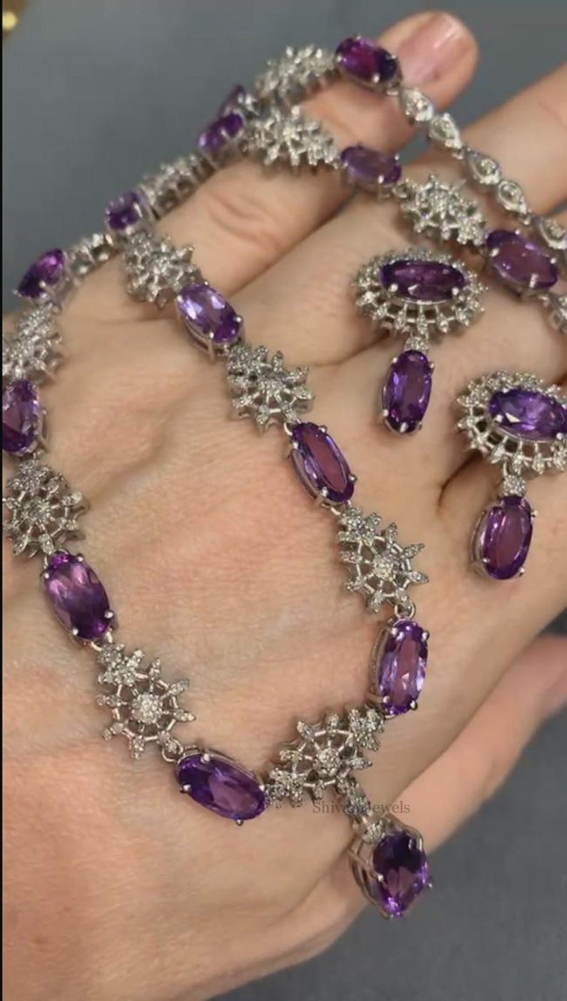 May include: A silver necklace and earrings set with purple amethyst stones and clear cubic zirconia accents. The necklace features a delicate snowflake design and the earrings are drop style.