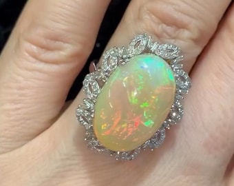 May include: A white opal ring with a delicate diamond halo setting. The opal is oval shaped and has a rainbow of colors.