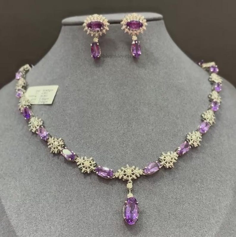May include: A purple amethyst necklace and earrings set with a delicate floral design. The necklace features a pendant with a larger oval-shaped amethyst.