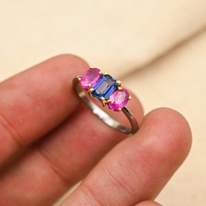 May include: A silver ring with three gemstones. The center stone is a rectangular blue sapphire, flanked by two oval pink sapphires.