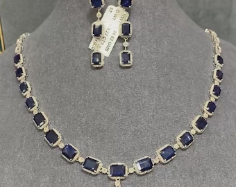 Pode incluir: Um conjunto de colar e brincos de ouro com um pingente e várias pedras preciosas azuis de forma quadrada. Os brincos são brincos pendentes com três pedras preciosas cada. O colar tem um total de 12 pedras preciosas. A etiqueta diz "SW 2.92 GMS, ST SIZE 14, 1.5 DWT".